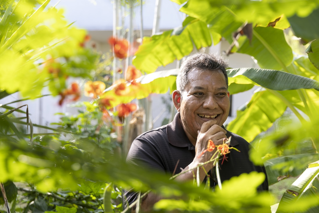 man sits among plants and a garden, smiling