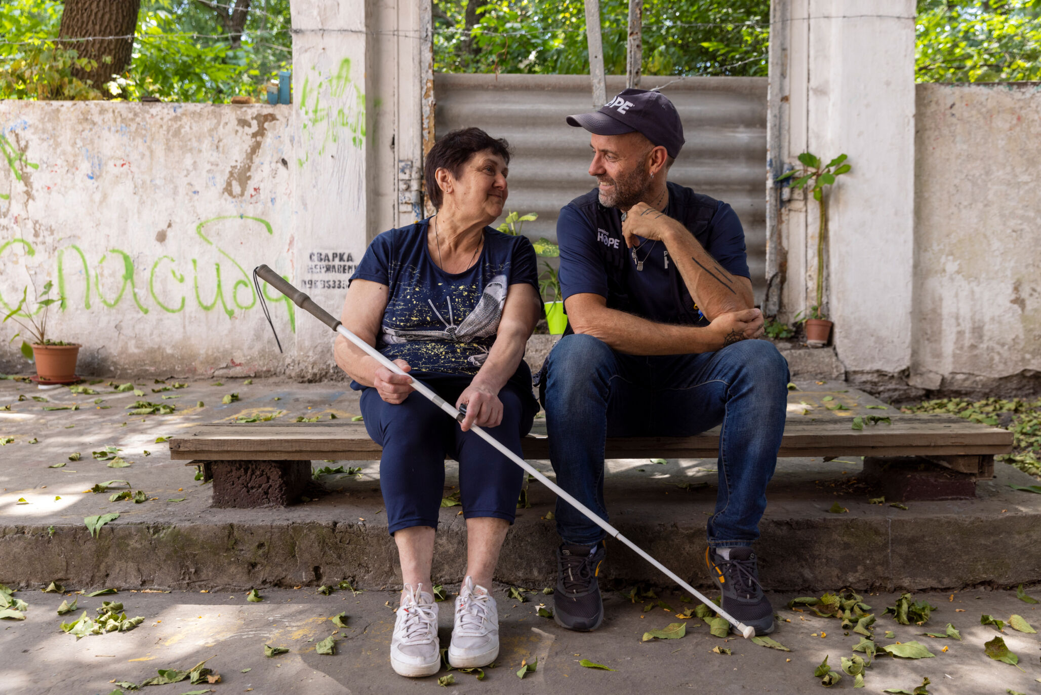 older blind woman sits next to man and they are smiling to each other