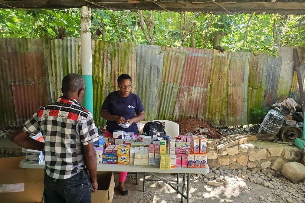 Woman in a Project HOPE shirt stands behind a table full of supplies to distribute to community members in Haiti