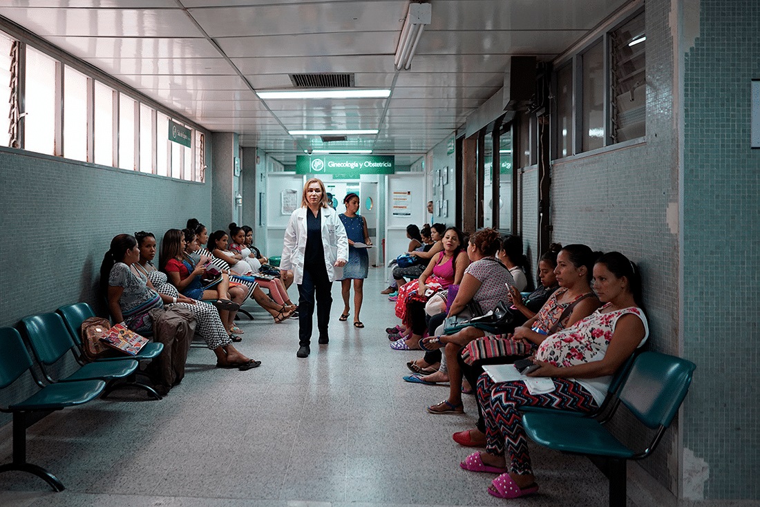medical staff walks down hospital hallway with pregnant women sitting on both sides waiting for treatment