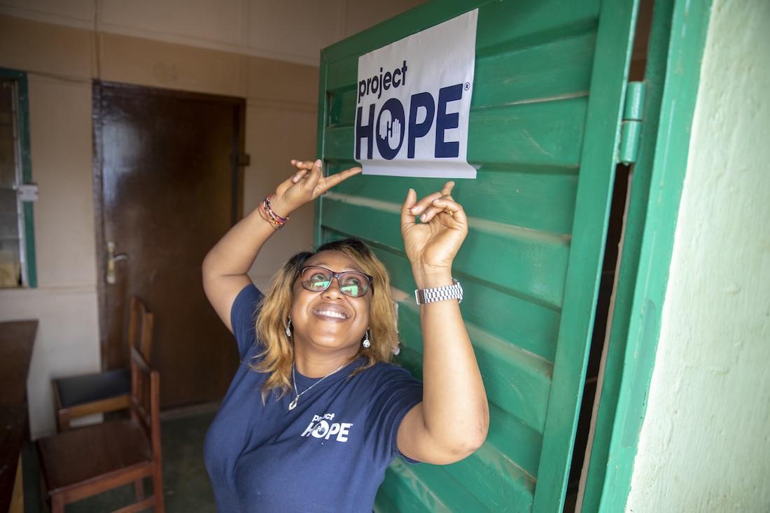 woman leans against door and points to sign reading Project HOPE above her