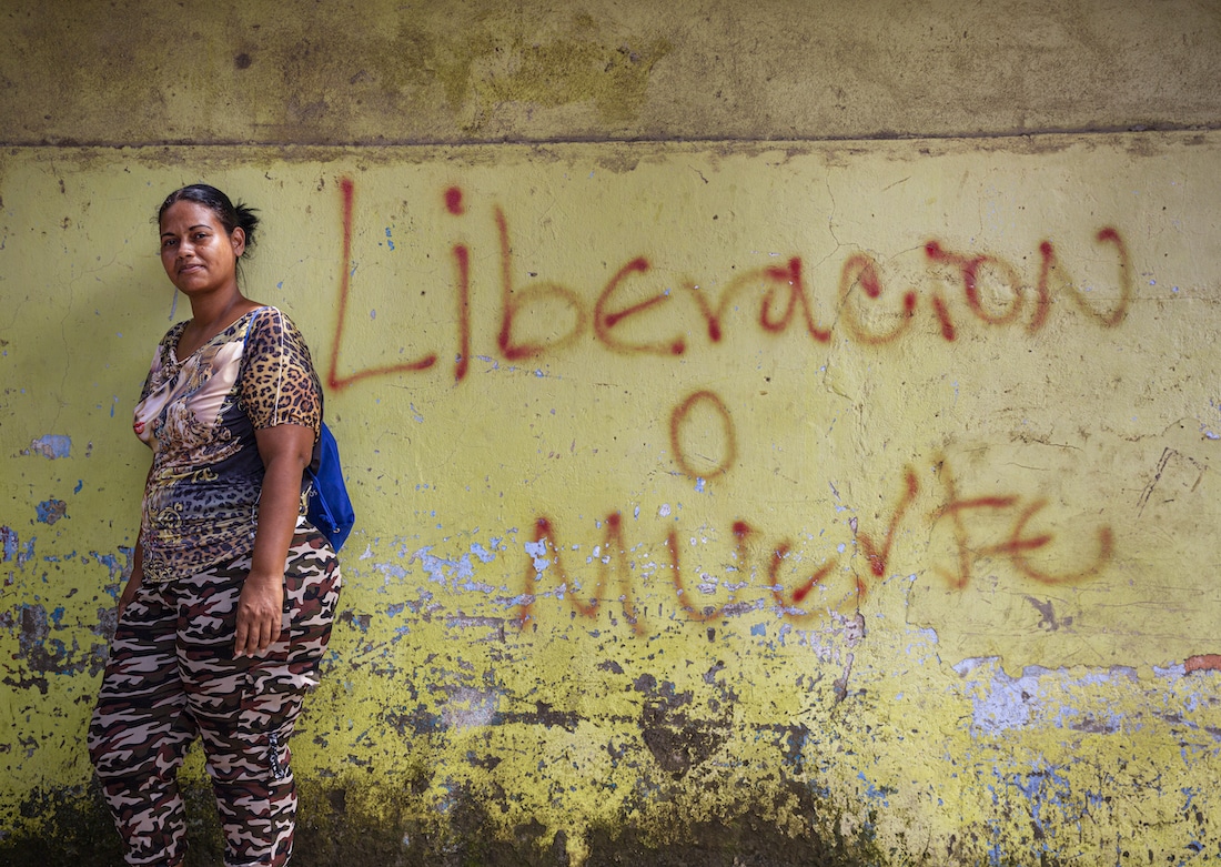 a woman in pink camo and leopard print stands in front of a yellow wall that reads in Spanish 