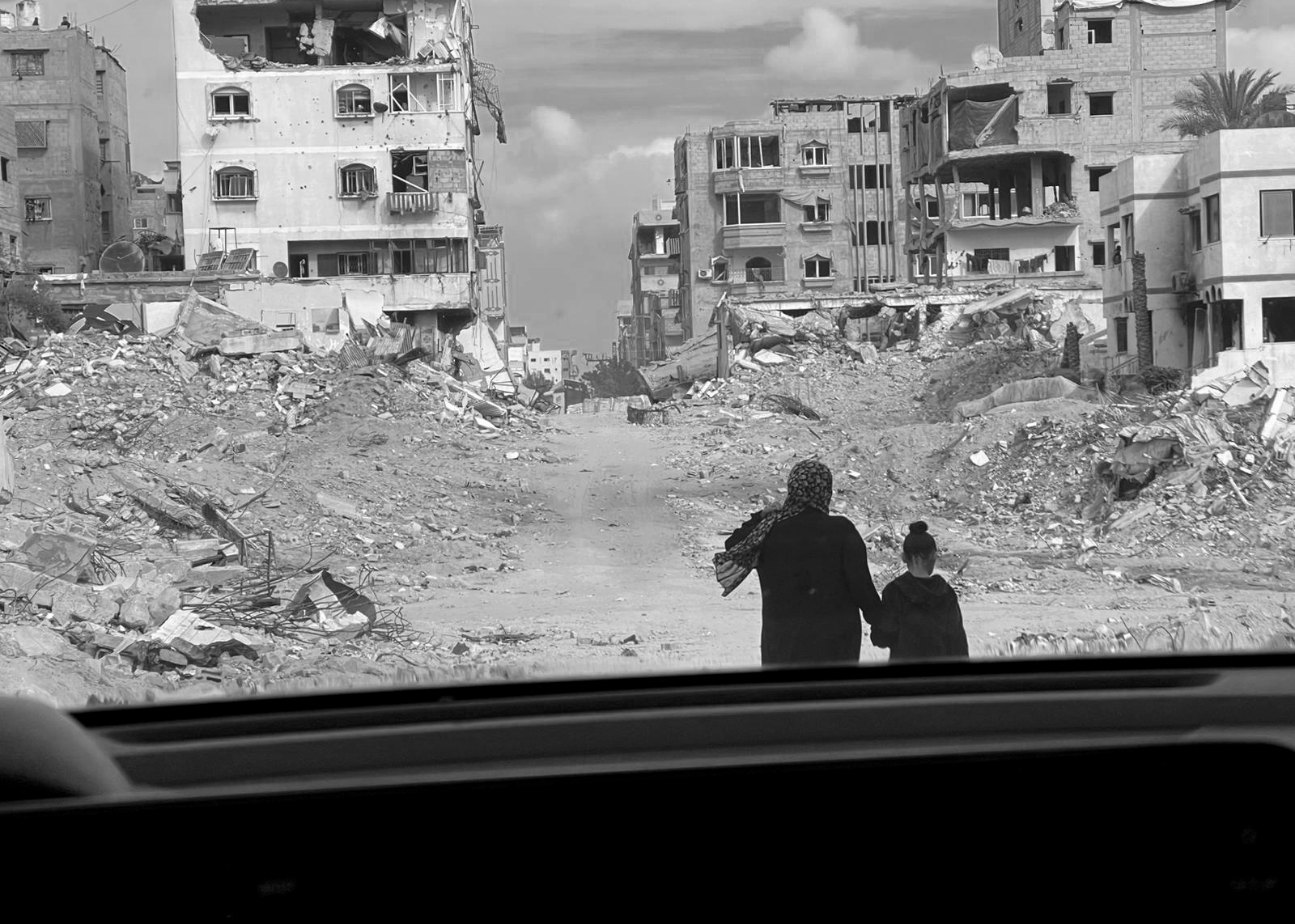 a mother and child walk through rubble in Gaza