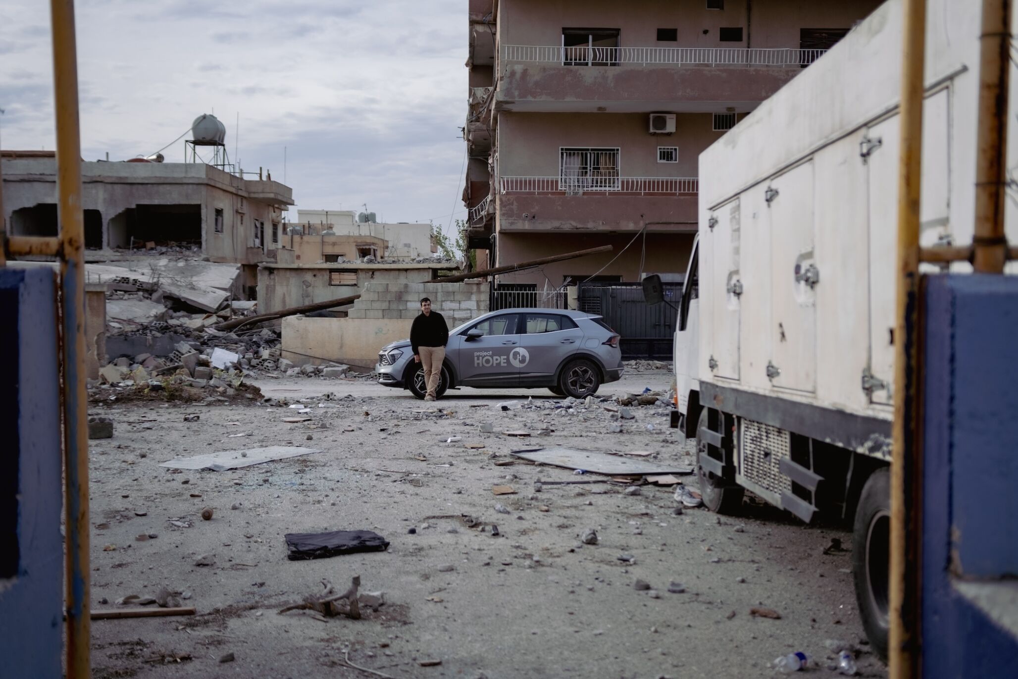 man leans against car while destroyed buildings are all around him