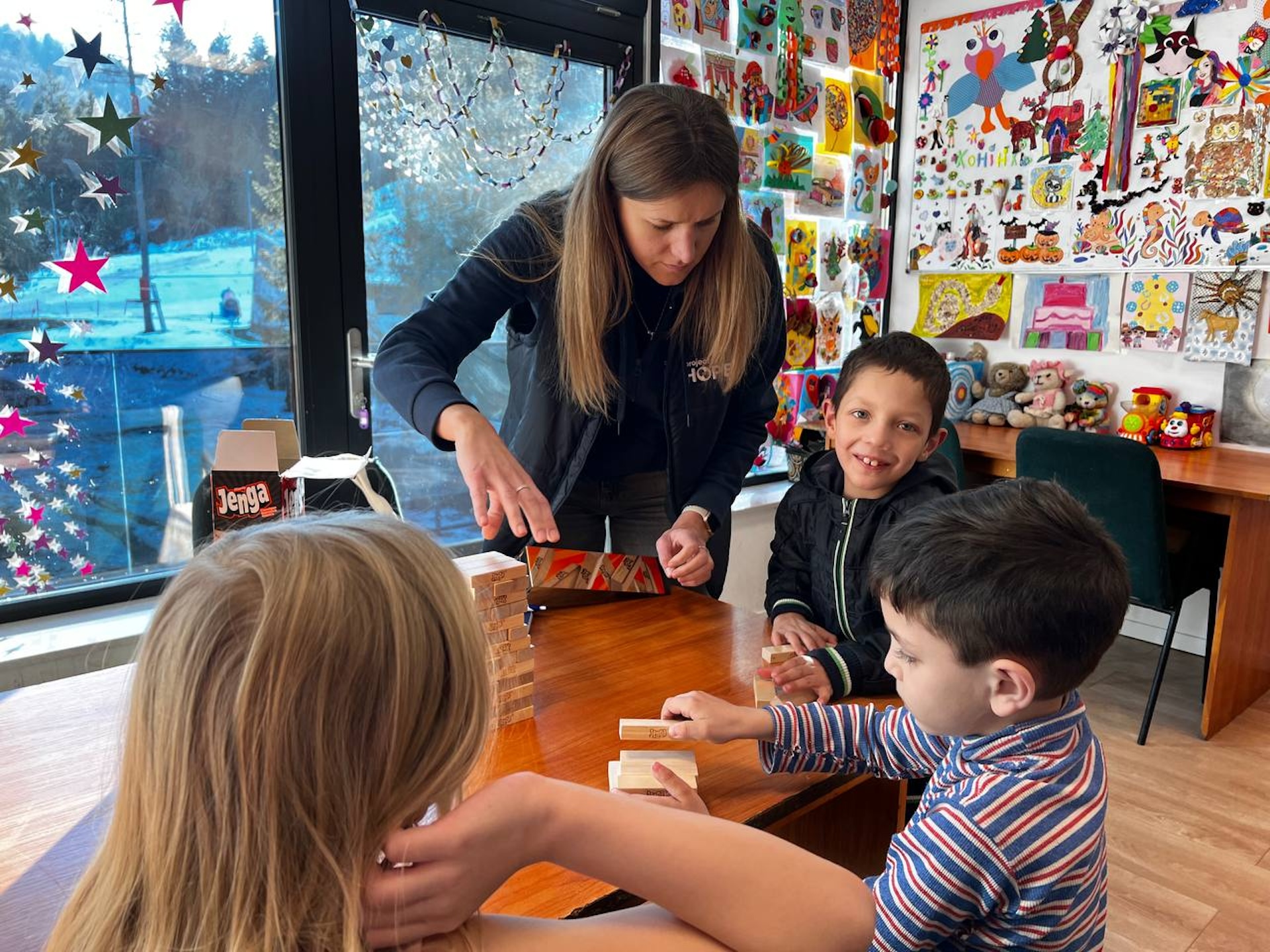 woman shows three young children how to play jenga